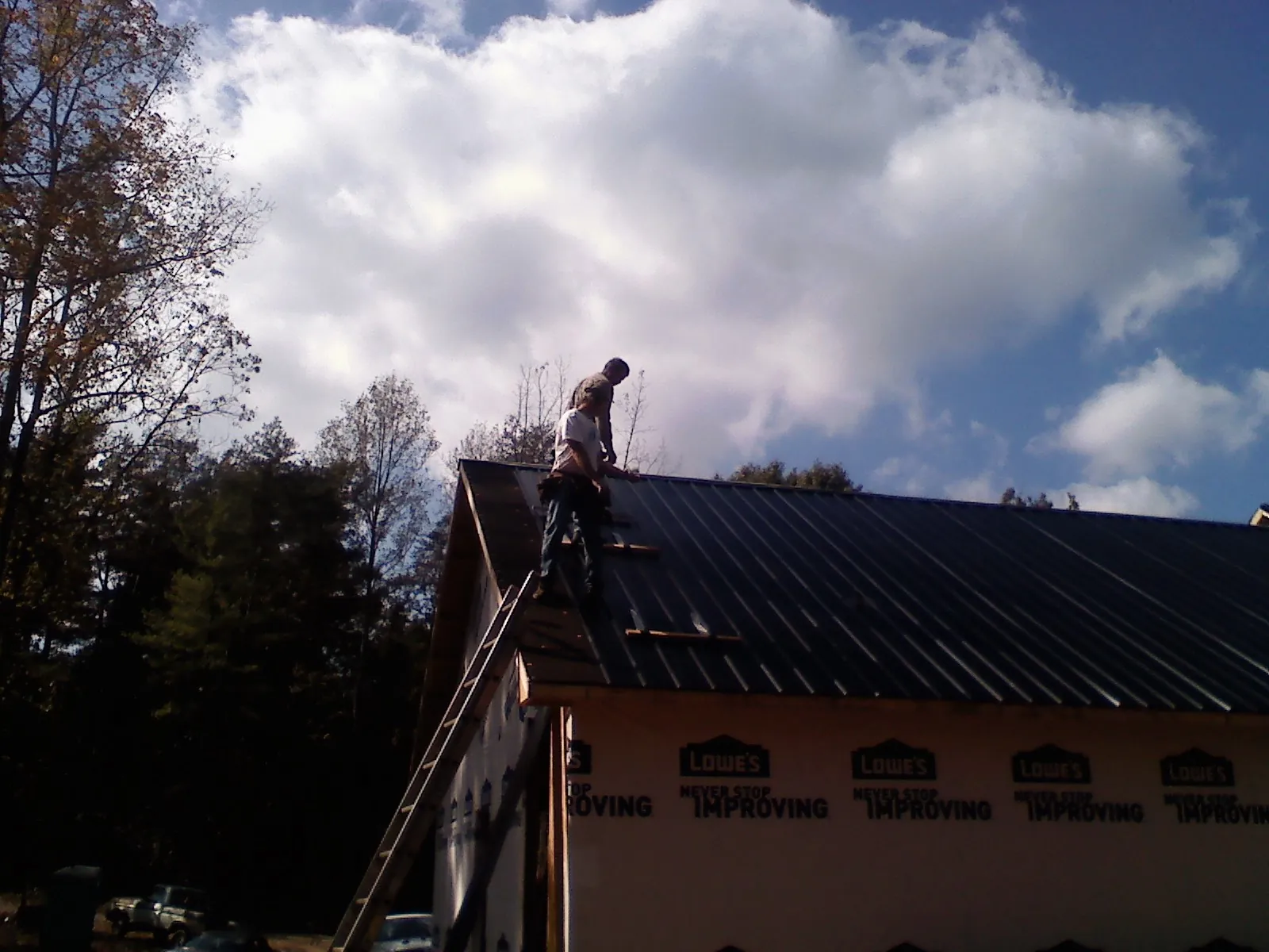 Roofer fastening dark metal panels high against a cloudy sky, from a Roof Inspection job in Benedict