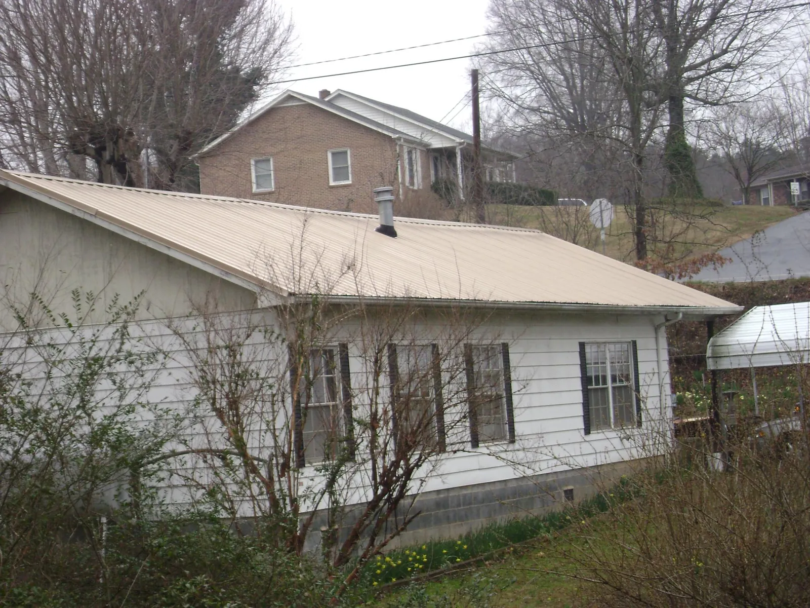 Tan metal roof on a white sided house set into a hillside — Commercial Roofing by Roofing Brothers in Benedict